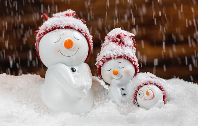 Three cute porcelain snowmen with red caps, in the snow