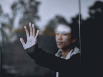 image on a man behind a window, with his hand stretched out to touch the glass